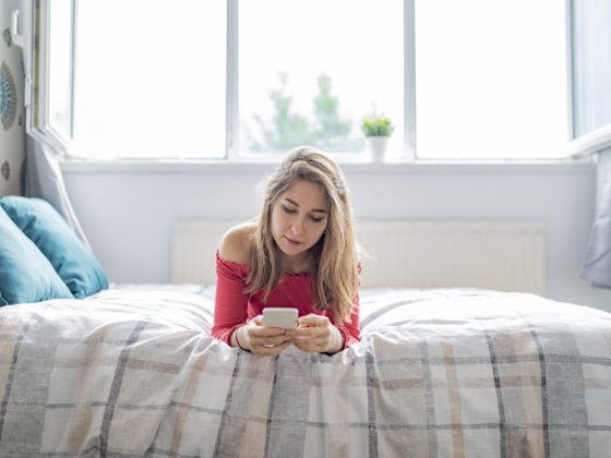 single woman looking at online dating profiles on her phone in bed