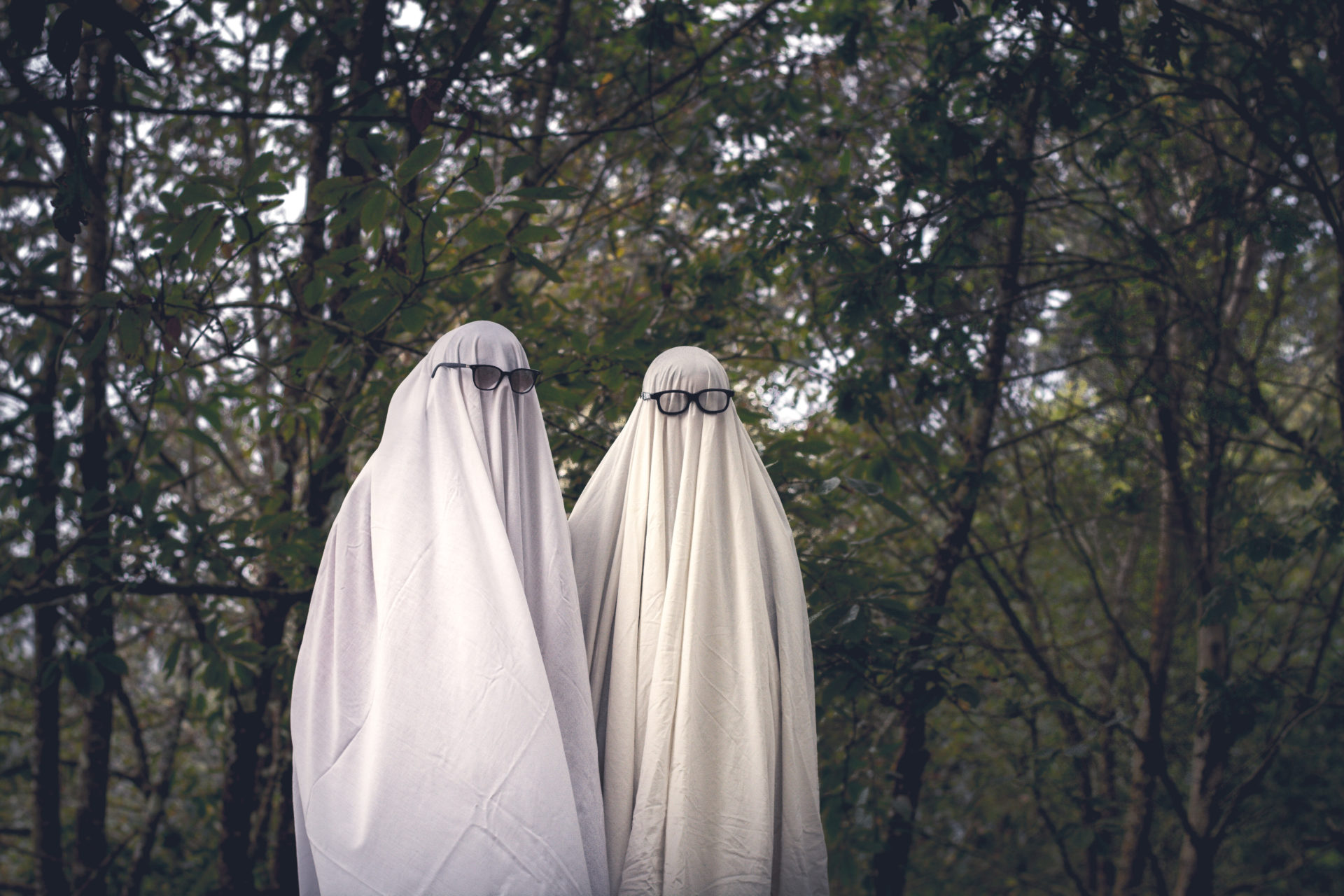 two people dressed as spooky ghosts walking outside in the forest